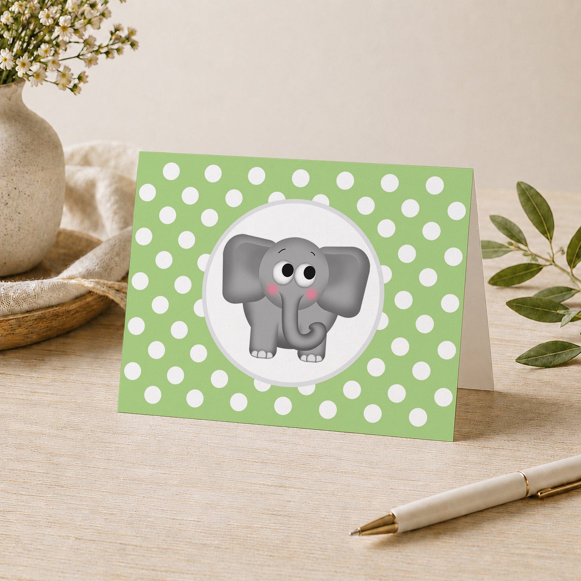 Cute Elephant Green Polka Dot Note Card shown on a desk with a vase, plants, and a pen.