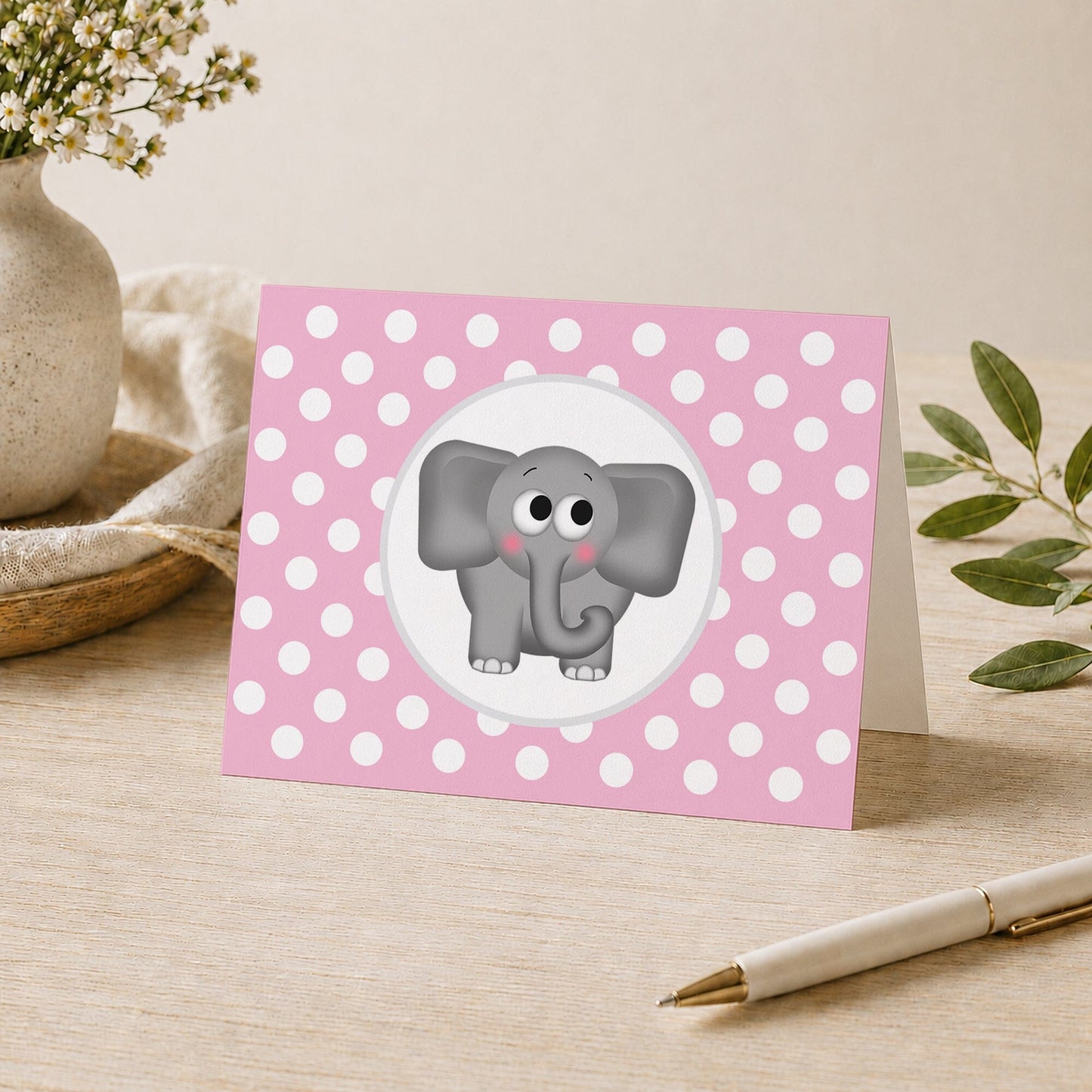 Cute Elephant Pink Polka Dot Note Card shown on a desk with a vase, plants, and a pen.