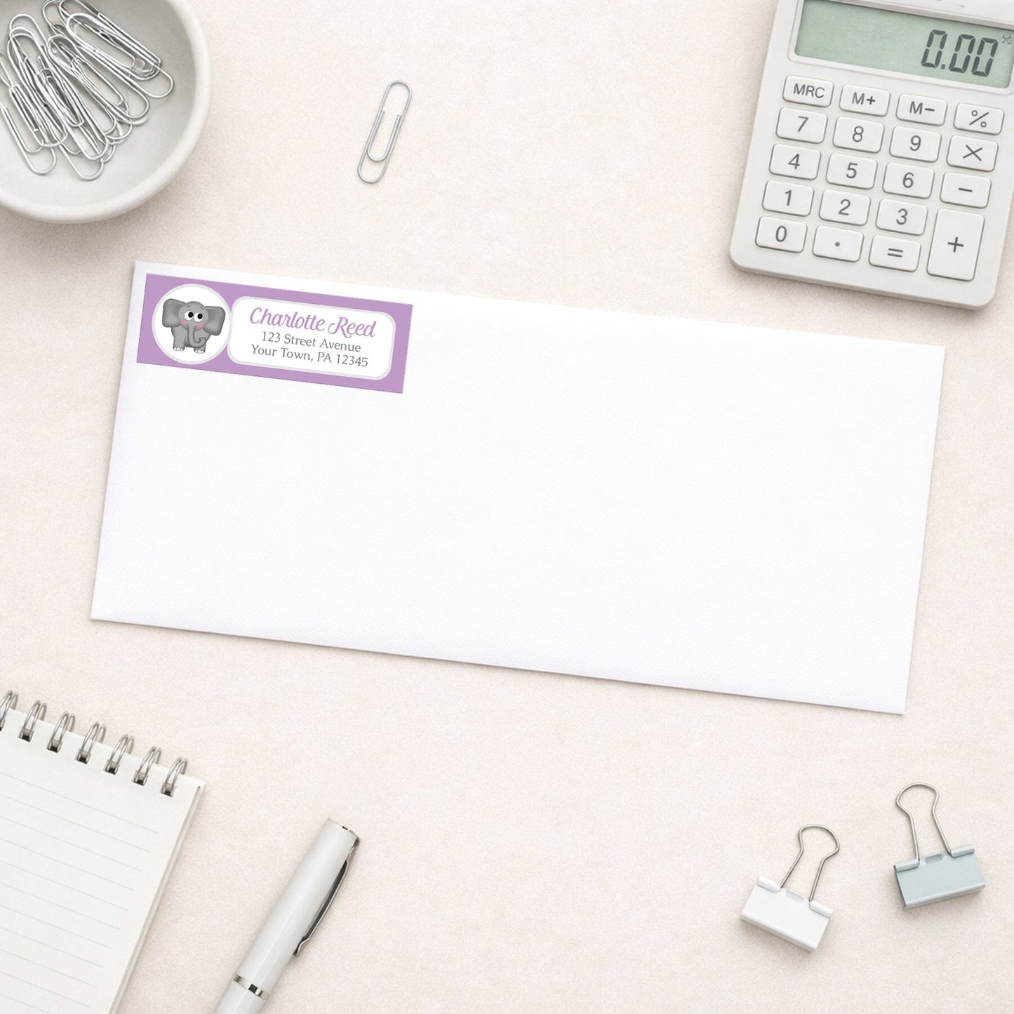 Cute Elephant Purple Address Label shown on a white envelope with everyday office supplies