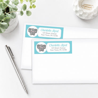 Address labels with a turquoise elephant design on white envelopes, shown on a white surface with a pen and plant.