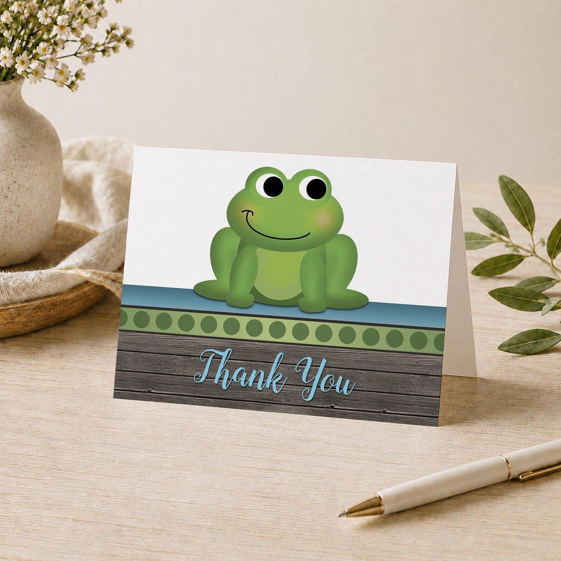 Cute Frog Green Rustic Wood Thank You Card shown on a tabletop with a vase, plants, and a pen.