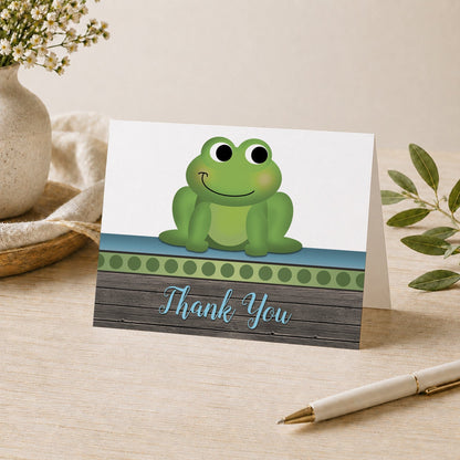 Cute Frog Green Rustic Wood Thank You Card shown on a tabletop with a vase, plants, and a pen.
