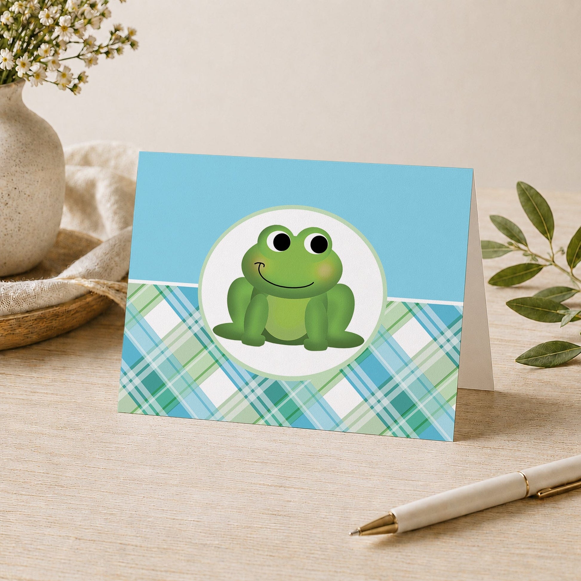 Cute Frog Green and Blue Plaid Note Card shown on a desk with a vase, plants, and a pen.