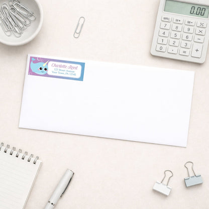 Cute Happy Narwhal Return Address Label shown on a white envelope with everyday office supplies