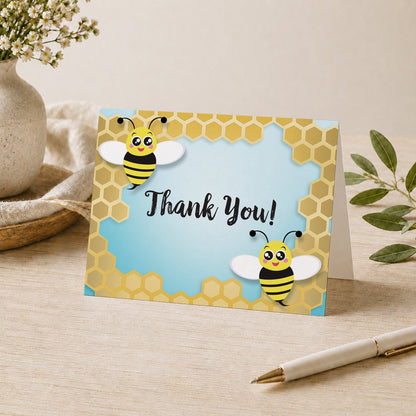 Cute Honeycomb Bee Thank You Card shown on a tabletop with a vase, plants, and a pen.