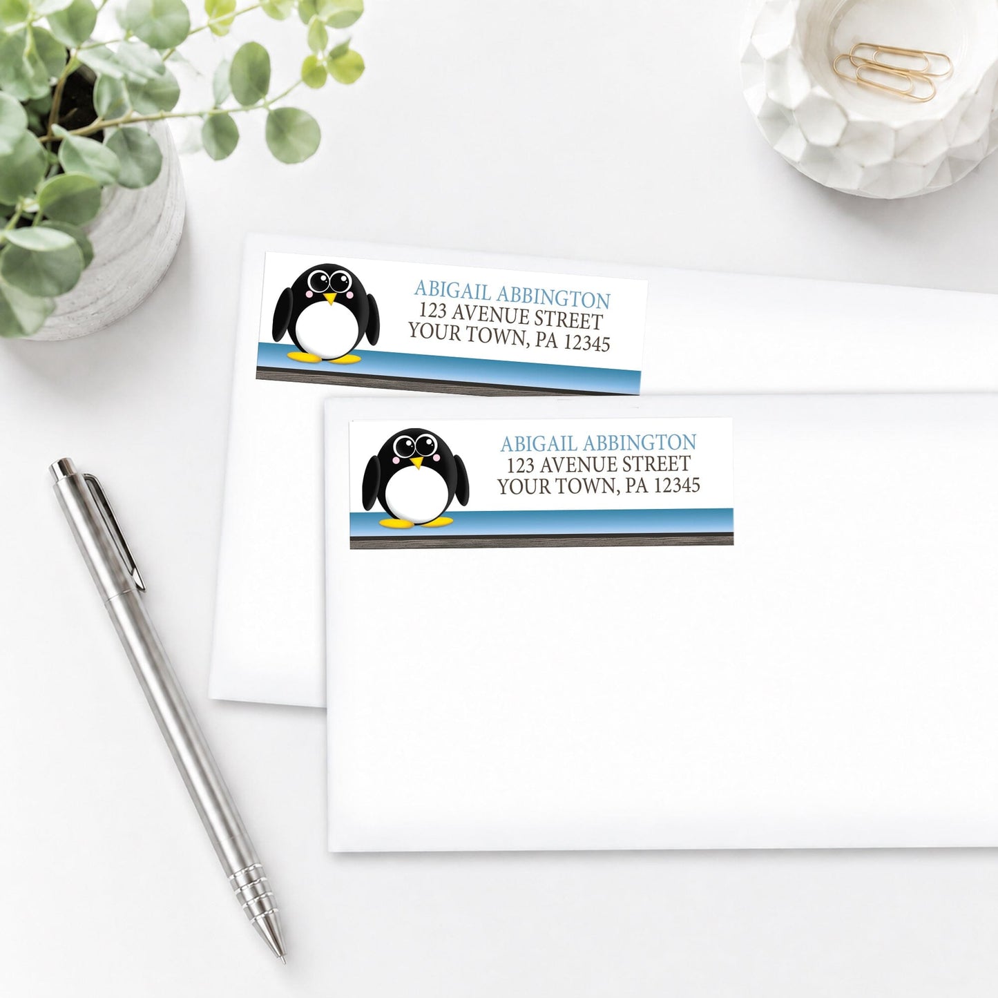Cute Penguin Blue Rustic Address Labels on white envelopes, shown on a white surface with a plant and a pen.
