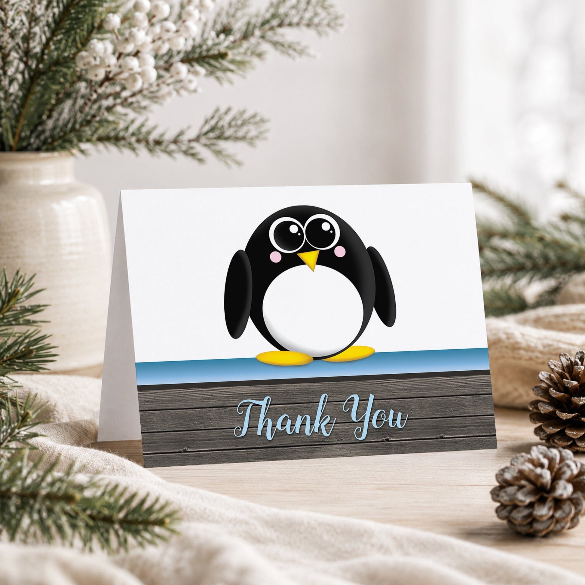 Cute Penguin Blue Rustic Wood Thank You Card shown on a tabletop with a vase, winter greenery, and pine cones.