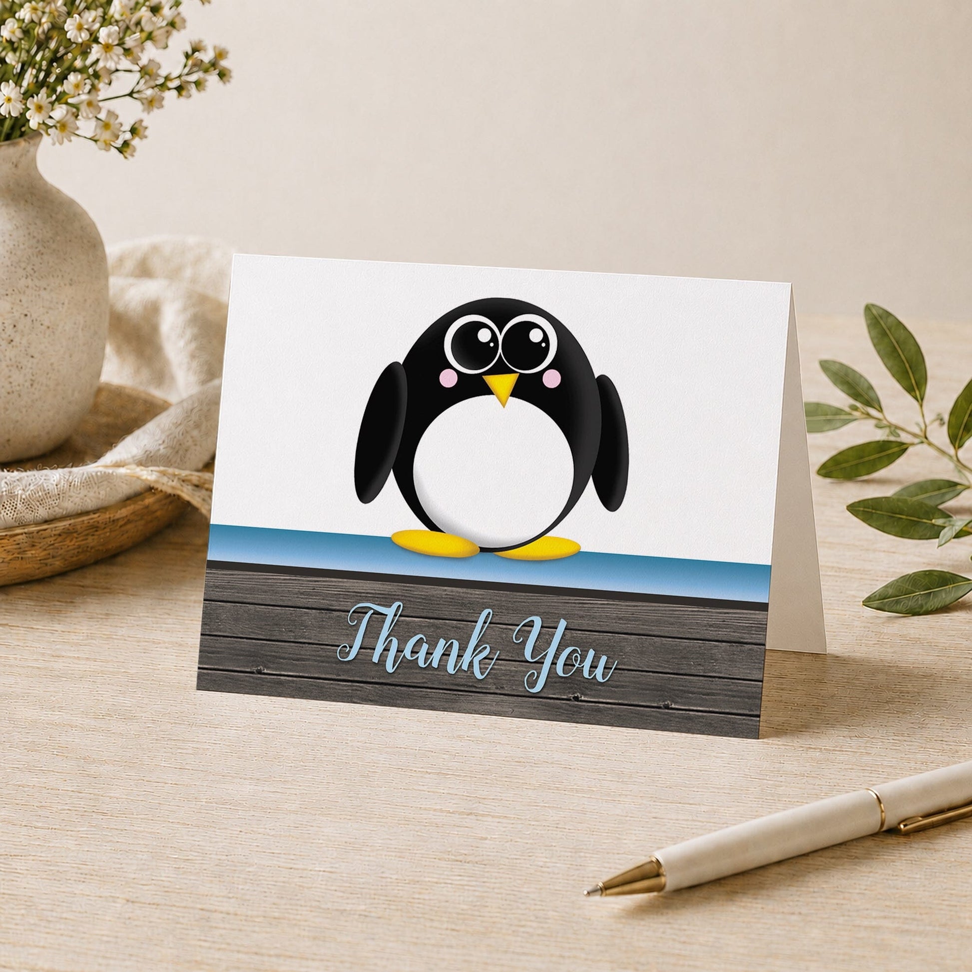 Cute Penguin Blue Rustic Wood Thank You Card shown on a desk with a vase, plants, and a pen.