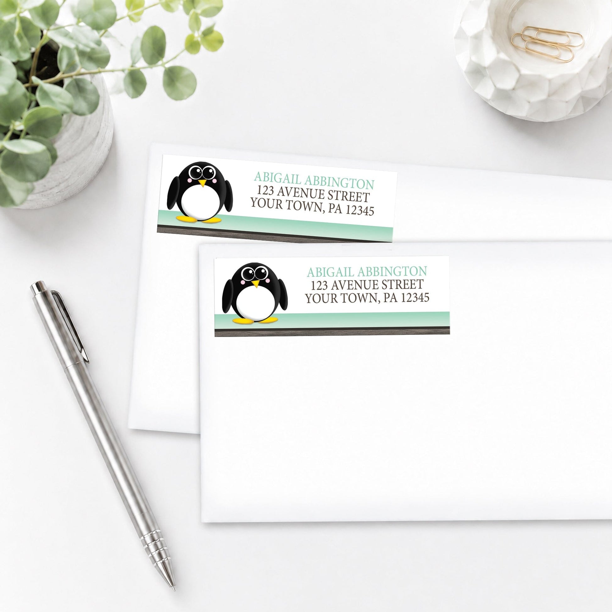 Two Cute Penguin Mint Green Rustic Address Labels on white envelopes, shown on a white surface with a pen and plant.