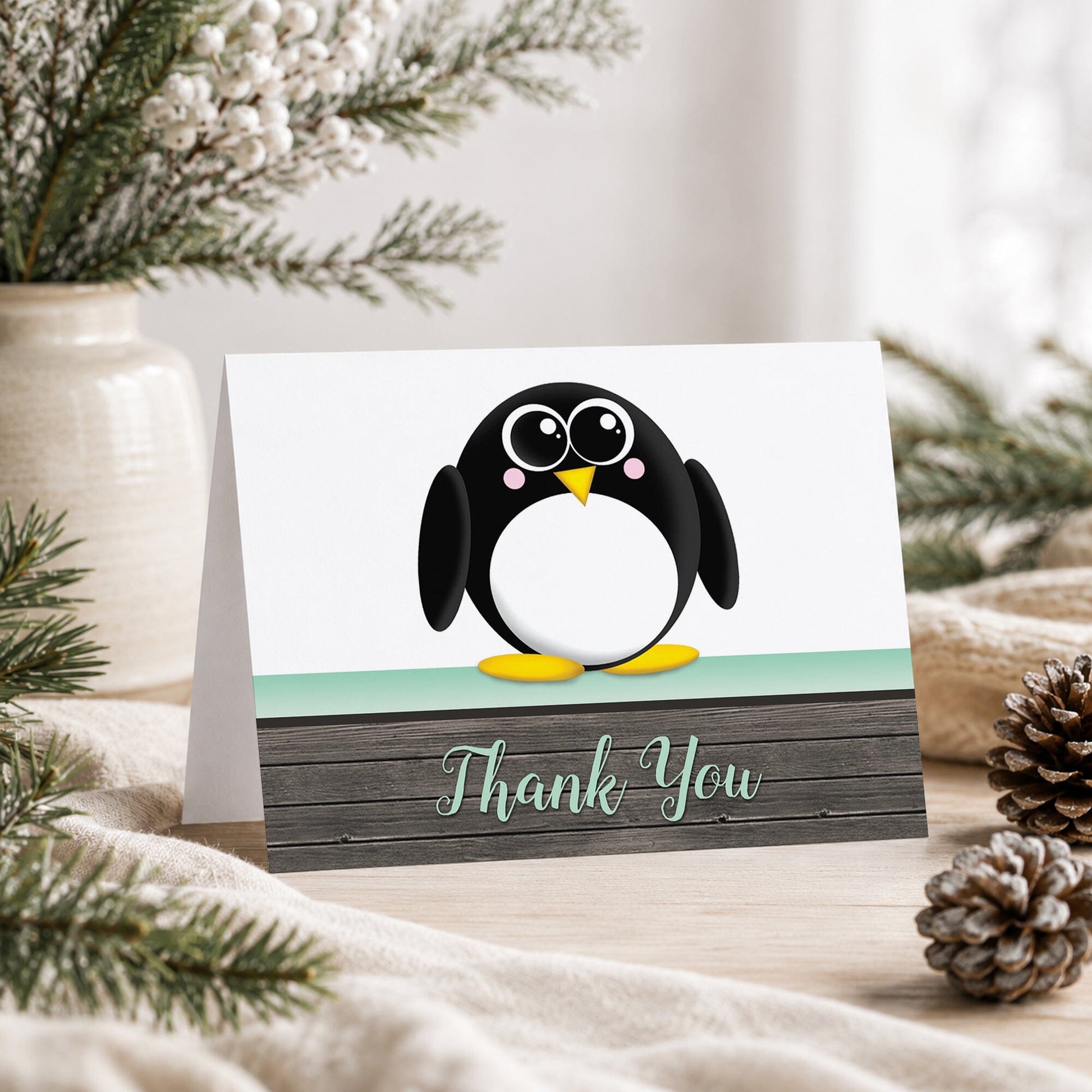 Cute Penguin Mint Green Rustic Wood Thank You Card shown on a tabletop with a vase, winter greenery, and pine cones.