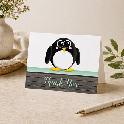 Cute Penguin Mint Green Rustic Wood Thank You Card shown on a desk with a vase, plants, and a pen.