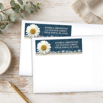 Address labels with daisy and denim design on white envelopes with a pen and eucalyptus branch on a wooden surface.