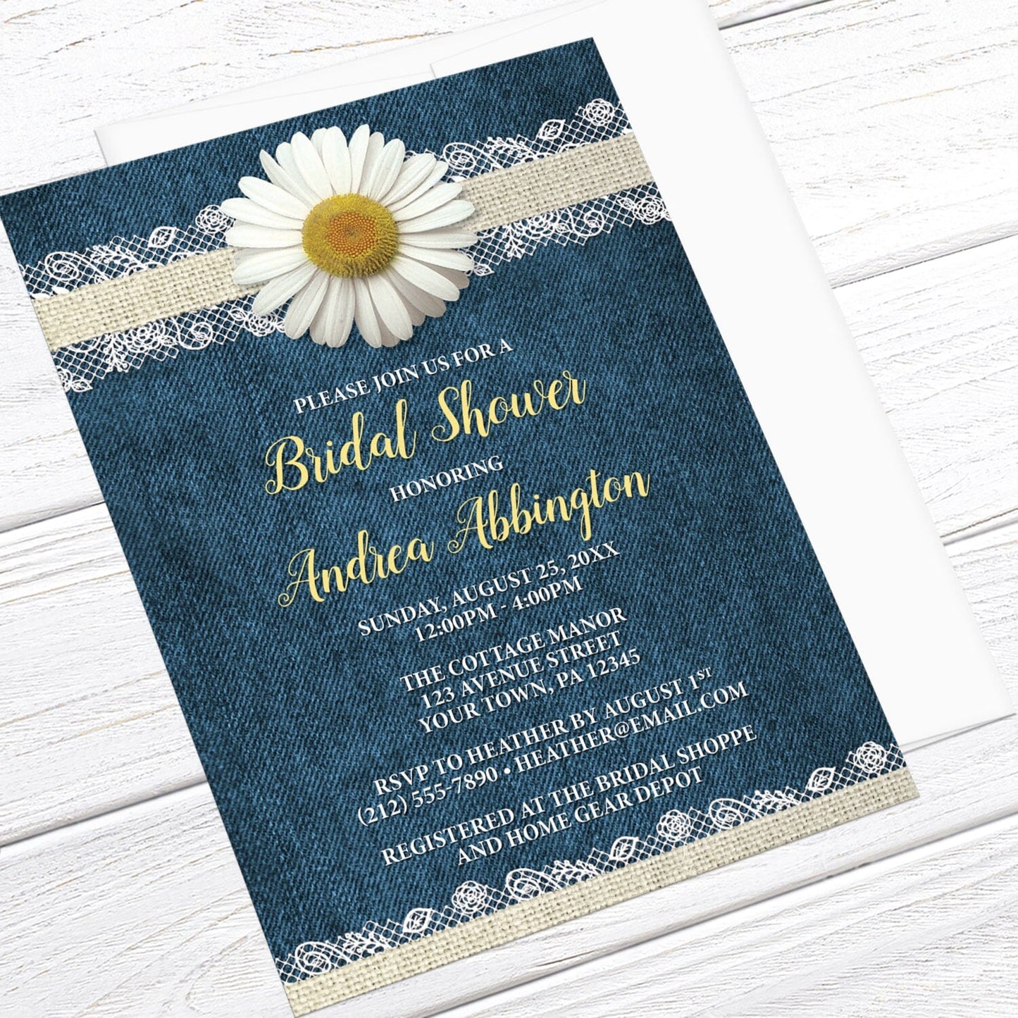 Daisy Burlap and Lace Denim Bridal Shower Invitation shown at an angle on a light wood surface with a white envelope.