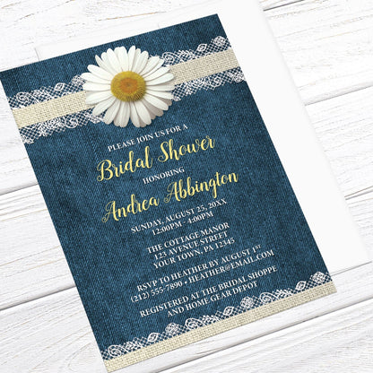 Daisy Burlap and Lace Denim Bridal Shower Invitation shown at an angle on a light wood surface with a white envelope.