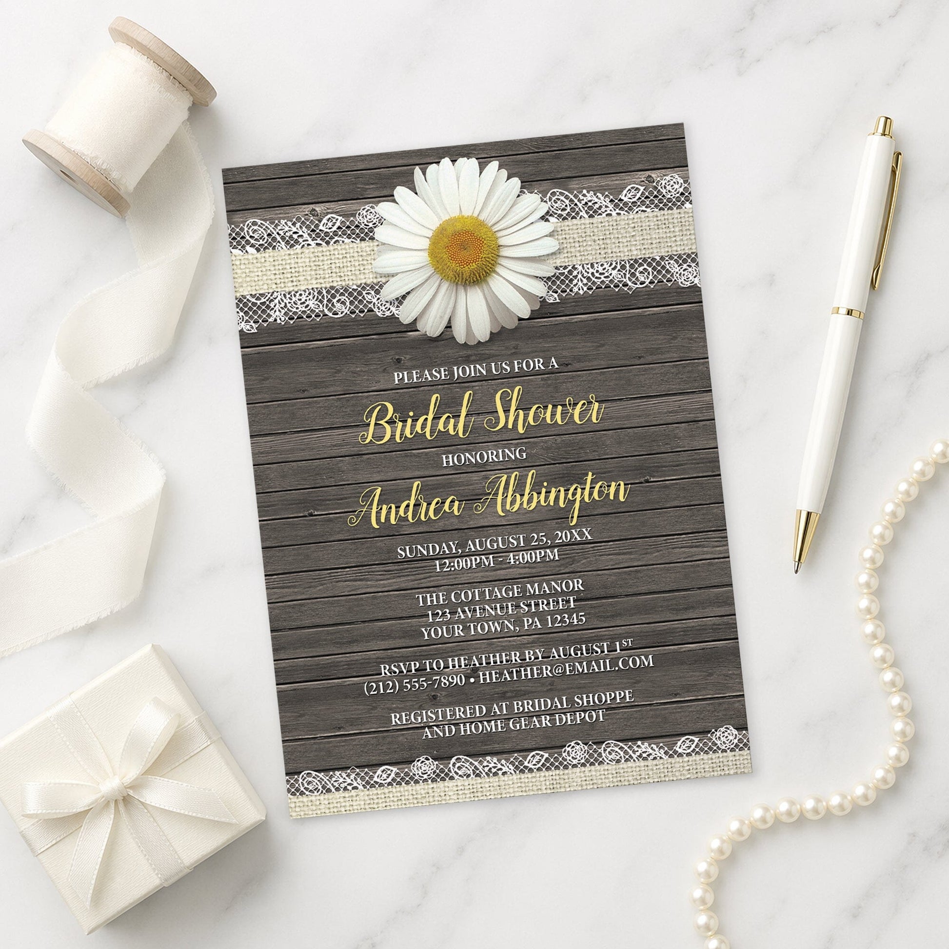 Bridal shower invitation with daisy and lace design on a wooden background, shown on a marble surface with decorative items.