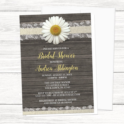 Floral bridal shower invitations with an illustrated design featuring a white dairy, burlap and lace, and a rustic wood background, displayed with a white envelope on a white wood surface