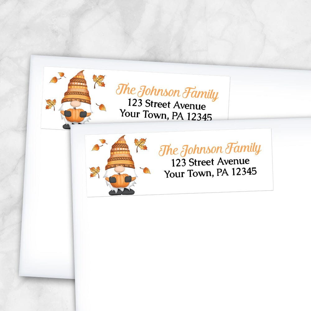 Fall Pumpkin Gnome Address Labels at Artistically Invited. Example of labels on envelopes. These address labels are designed with an illustration of a cute gnome holding an orange pumpkin with autumn leaves around him. Your personalized return address is custom printed in orange and black over white to the right of the autumn-themed gnome.