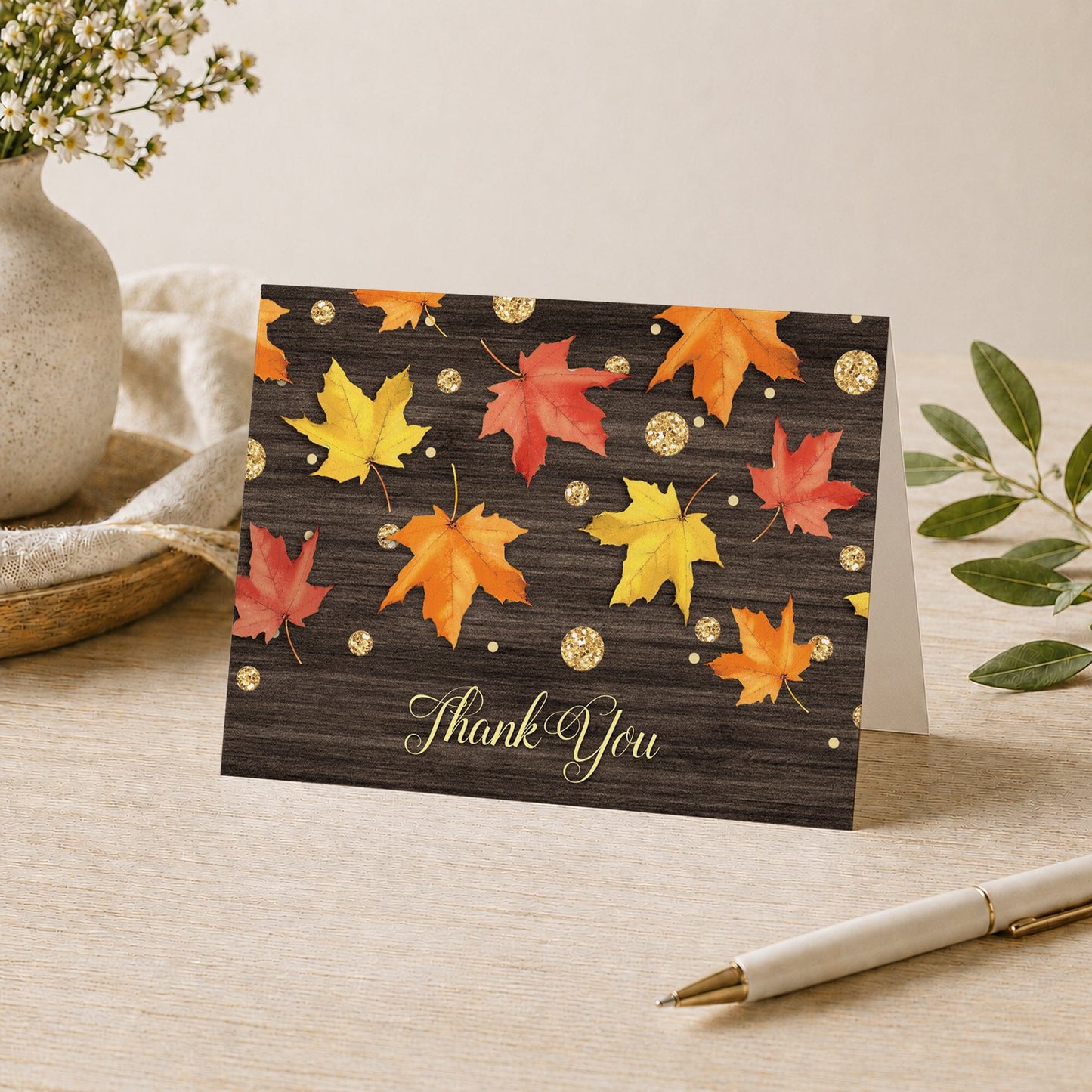 Falling Leaves with Gold Autumn Thank You Card shown on a desk with a vase, plants, and a pen.