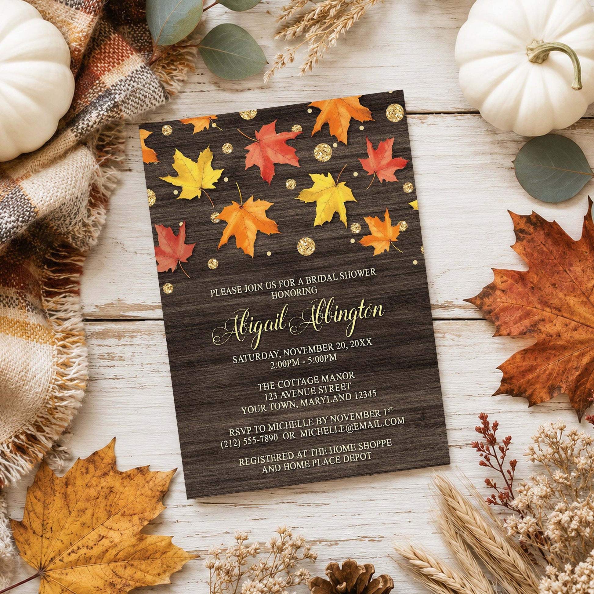 Falling Leaves with Gold Autumn Bridal Shower Invitation on a light wooden surface with fall leaves and autumn decor.