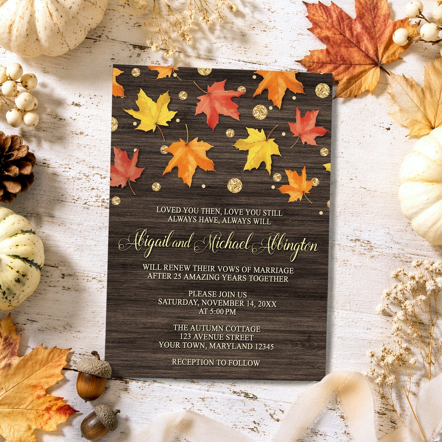 Falling Leaves with Gold Autumn Vow Renewal Invitation on a light wooden surface with fall leaves, pumpkins, and autumn decor.