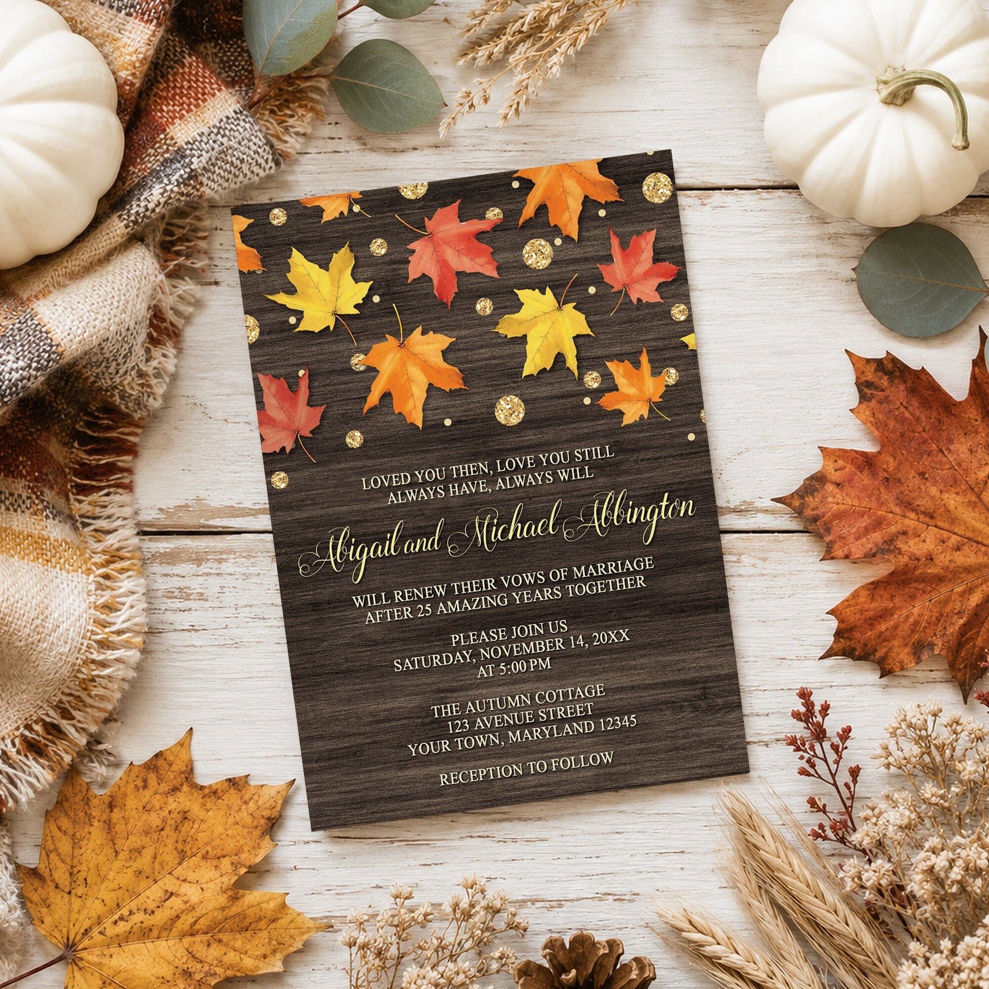 Falling Leaves with Gold Autumn Vow Renewal Invitation on a light wooden surface with fall leaves and autumn decor.