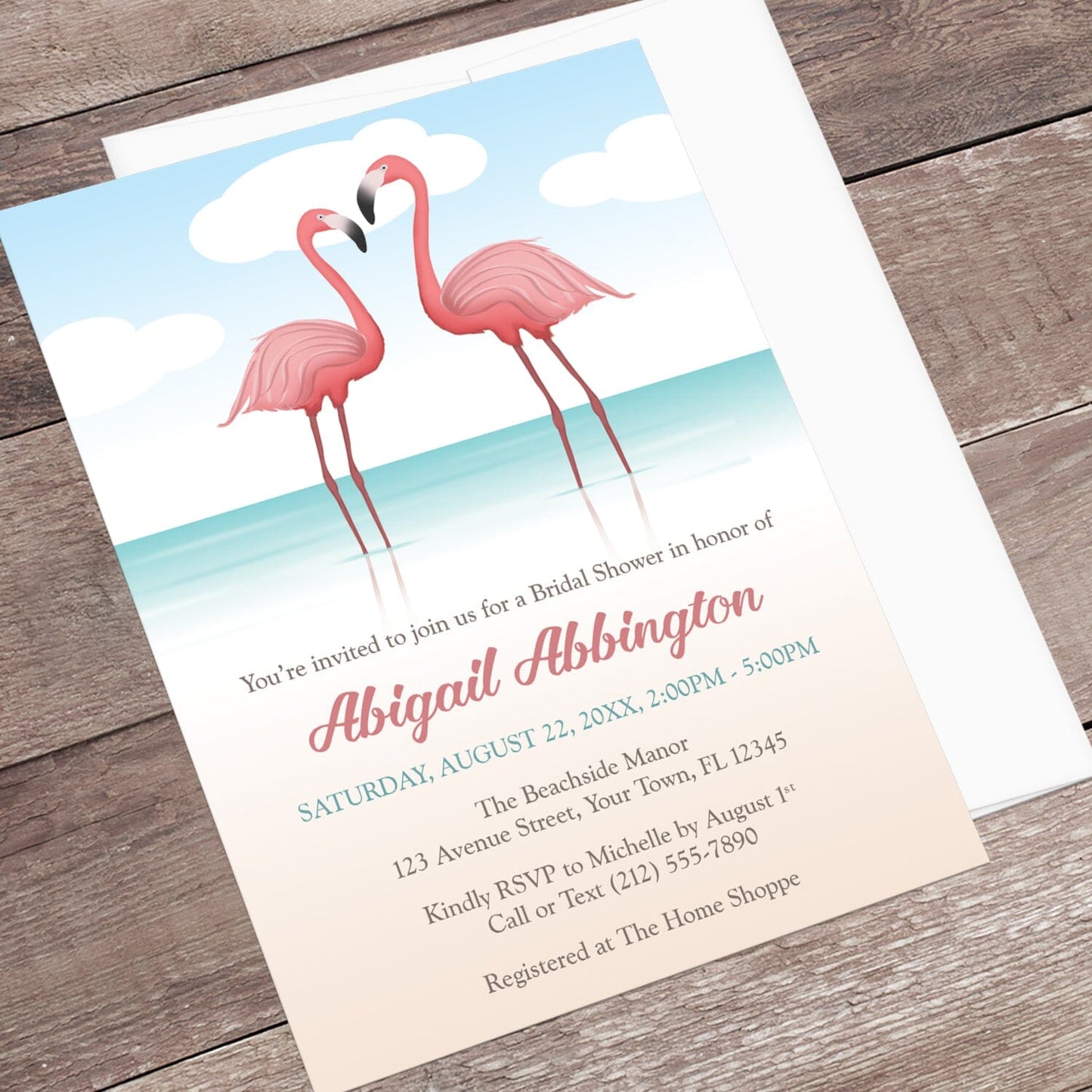 Flamingo-themed bridal shower invitation displayed at an angle with a white envelope on a wooden surface