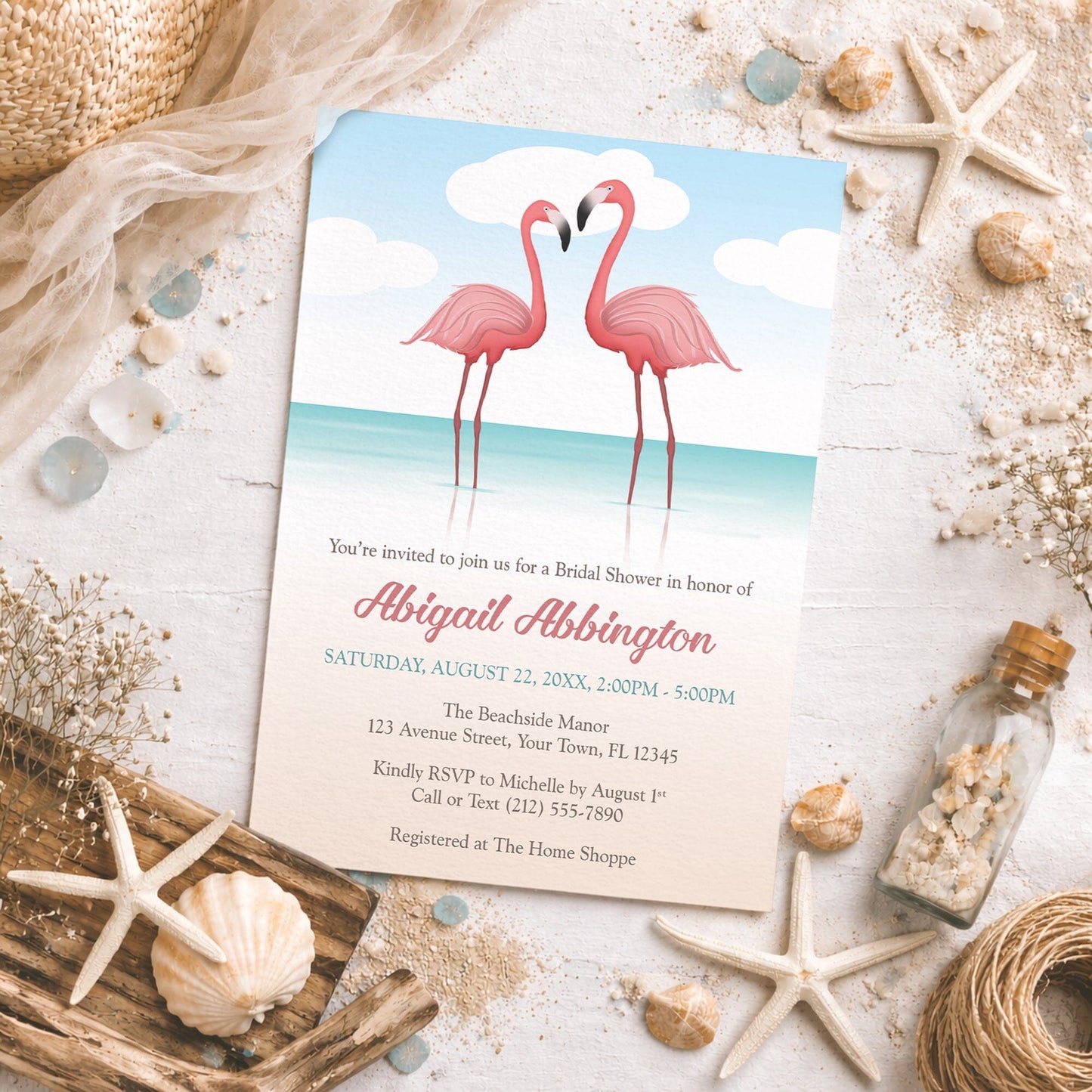Flamingos in the Water Bridal Shower Invitation on a rustic surface with seashells, sand, drift wood, and other beach decor.