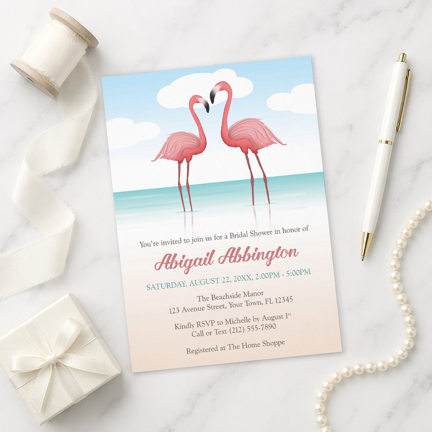 Flamingos in the Water Bridal Shower Invitation on a marble surface with a white gift box, ribbon, pen, and pearls.