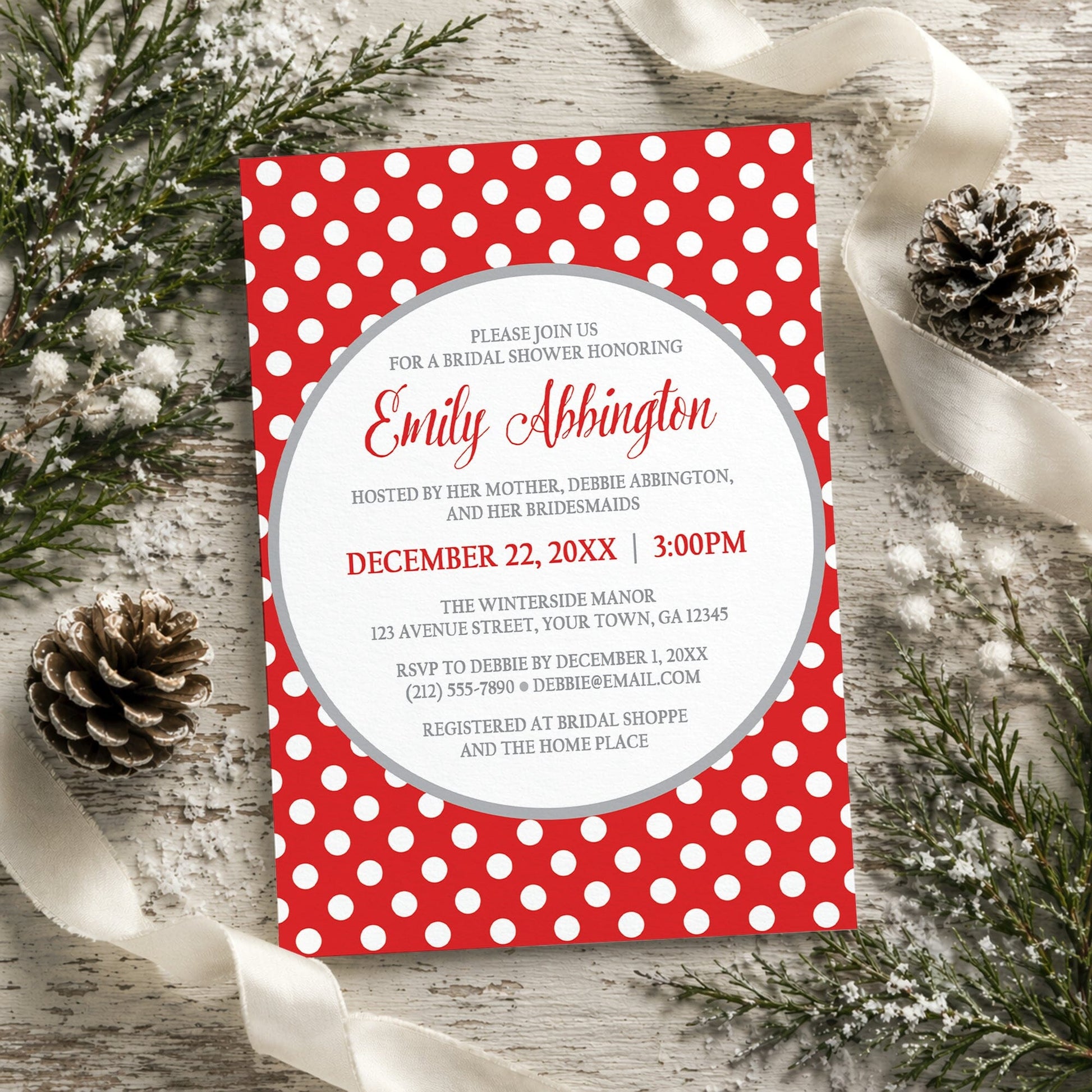 Gray and Red Polka Dot Bridal Shower Invitation shown on a rustic wooden surface with winter greenery, pine cones, and ribbons.