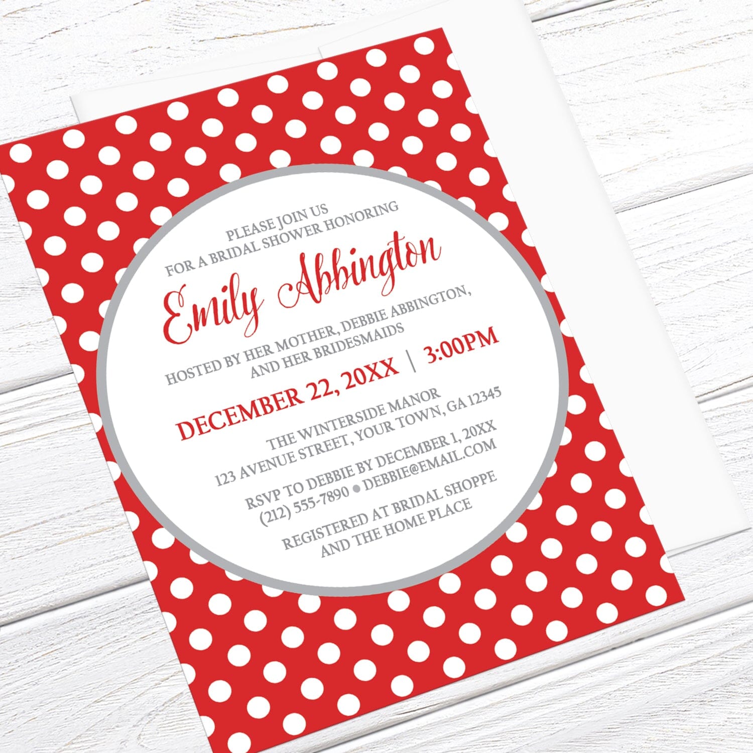 Gray and Red Polka Dot Bridal Shower Invitation shown at an angle on a light wood surface with a white envelope.