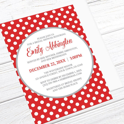 Gray and Red Polka Dot Bridal Shower Invitation shown at an angle on a light wood surface with a white envelope.