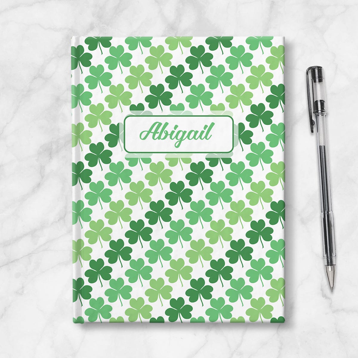Personalized Green Clovers Pattern Journal at Artistically Invited. Image shows the book on a countertop next to a pen.