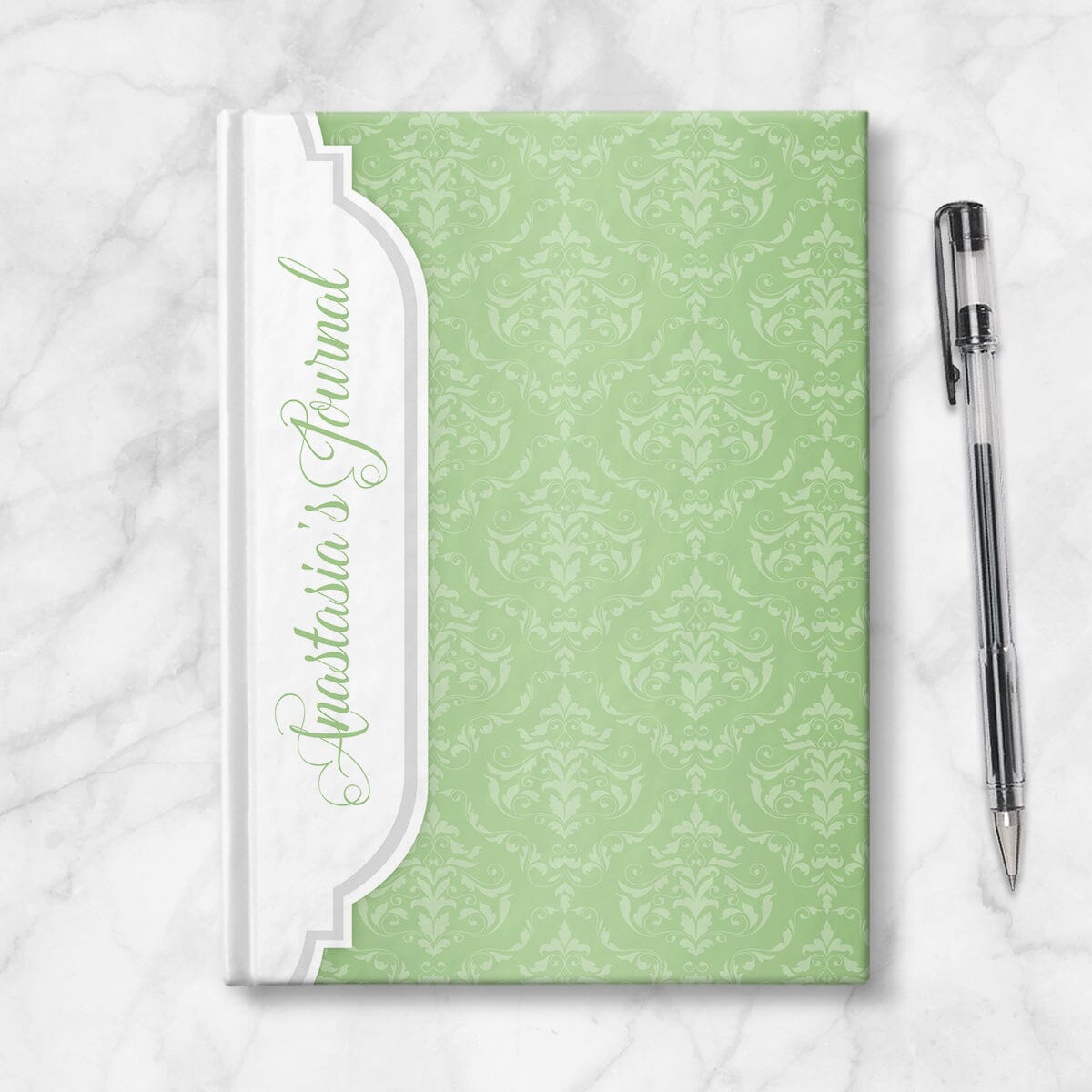 Personalized Green Damask Journal at Artistically Invited. Image shows the book on a countertop next to a pen.
