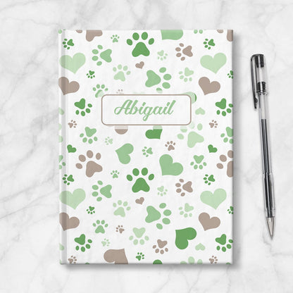 Personalized Green Hearts and Paw Prints Journal at Artistically Invited. Image shows the book on a countertop next to a pen.