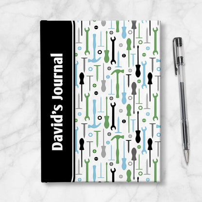 Personalized Green Blue Tools Pattern Journal at Artistically Invited. A custom book designed with a black color block wrapping around the spine area over an organized pattern of green, blue, black, and gray tools on the rest of the background. This handyman or contractor-inspired pattern includes hammers, screwdrivers, wrenches, nails, screws, and washers. Your personalized name and text of your choice is custom printed sideways in white over the black color block on the front near the spine.