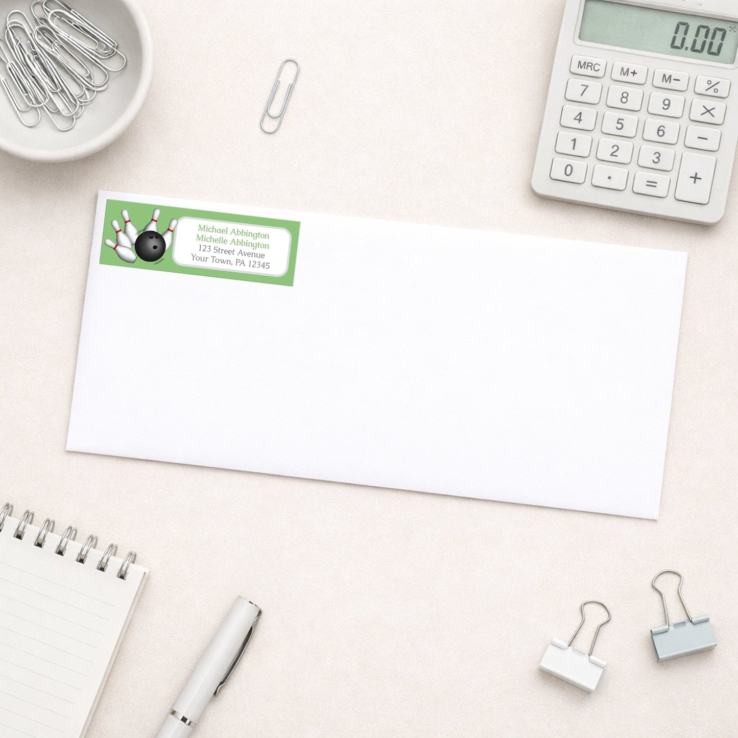 Green Bowling Return Address Label shown on a white envelope with everyday office supplies