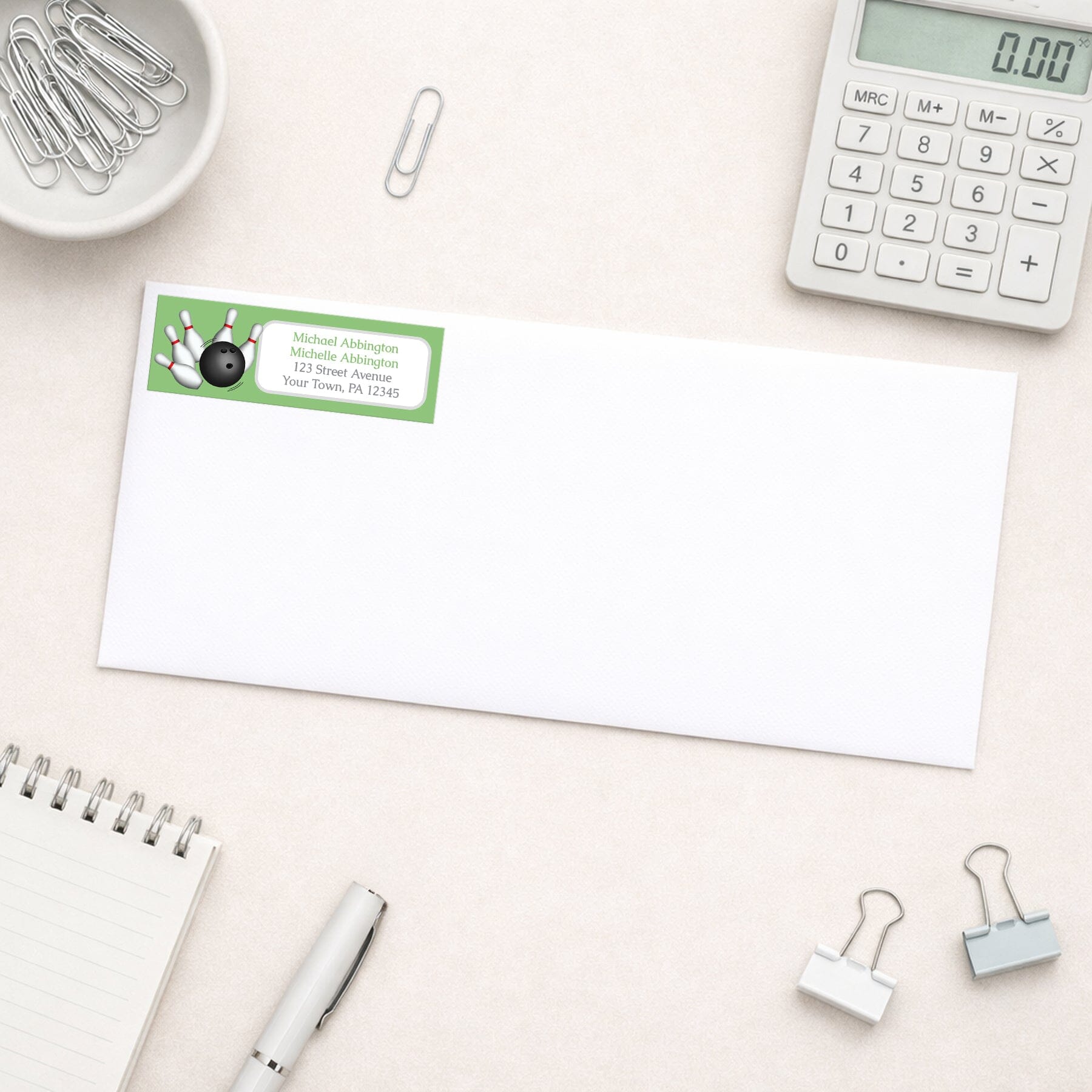 Green Bowling Return Address Label shown on a white envelope with everyday office supplies