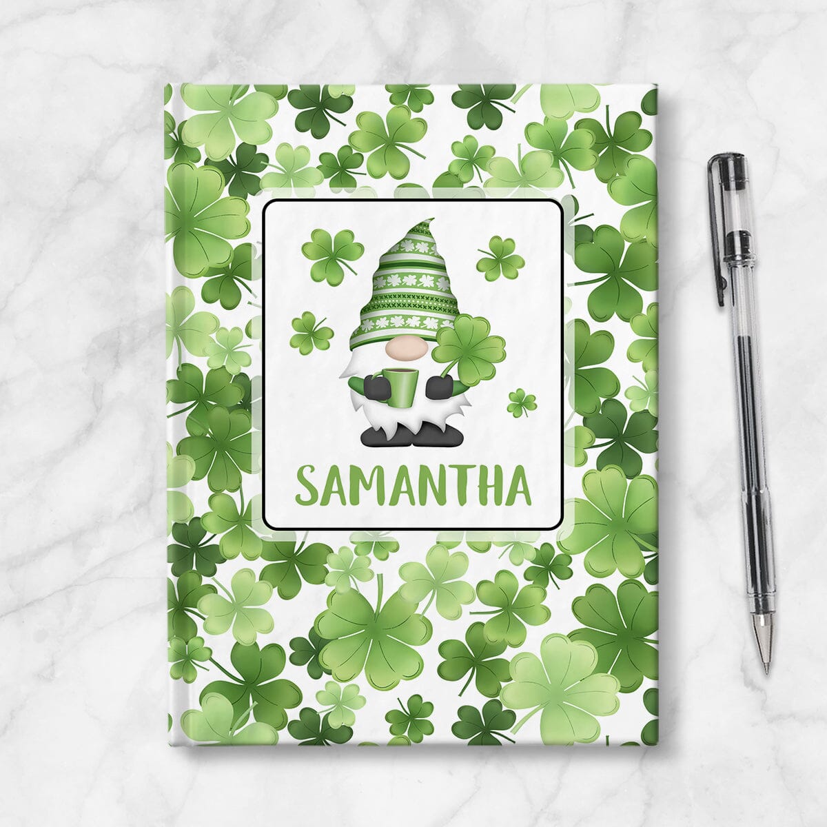 Personalized Green Shamrocks Gnome Journal at Artistically Invited. A custom book designed with an adorable gnome holding a hot beverage and a 4-leaf clover with 4 shamrocks floating around him in a white rectangular design on the front of the book, with your name personalized in green in a cute all capital letters font below the gnome. The background design that wraps around the cover of the book features a pattern of shamrocks and 4-leaf clovers in different shades of green. Book is next to a pen.