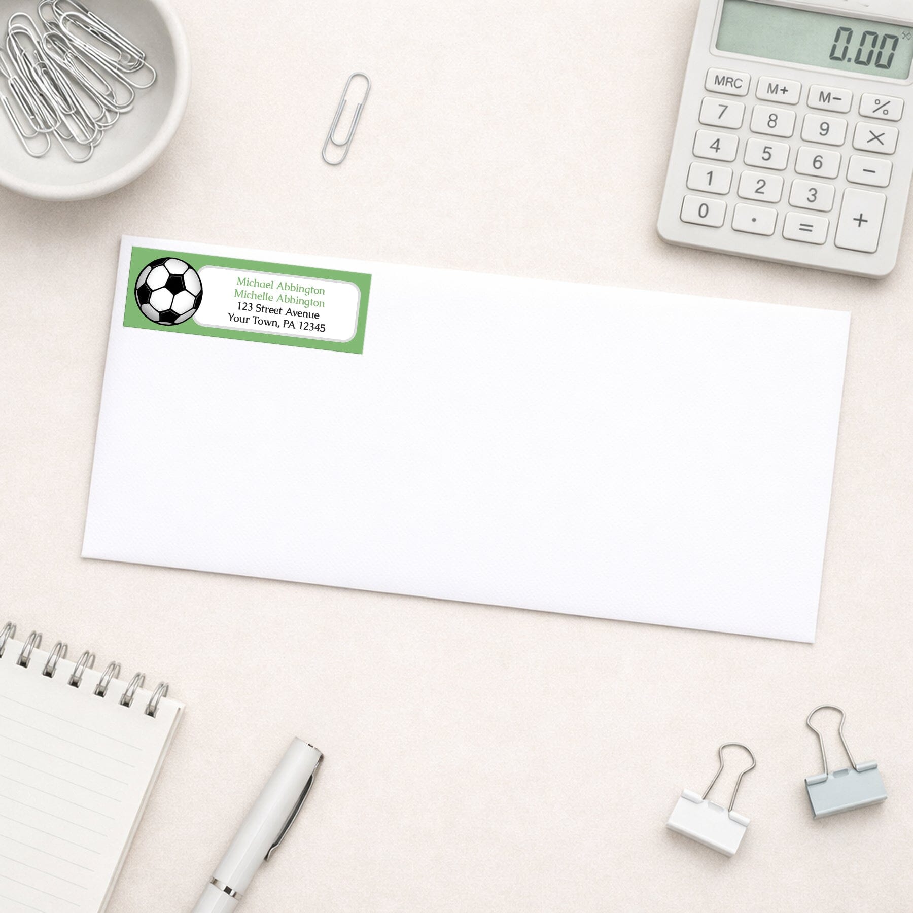 Green Soccer Ball Return Address Label shown on a white envelope with everyday office supplies