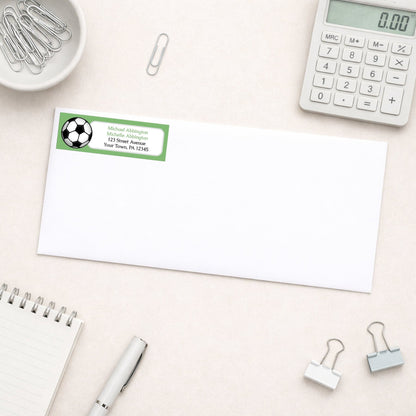 Green Soccer Ball Return Address Label shown on a white envelope with everyday office supplies