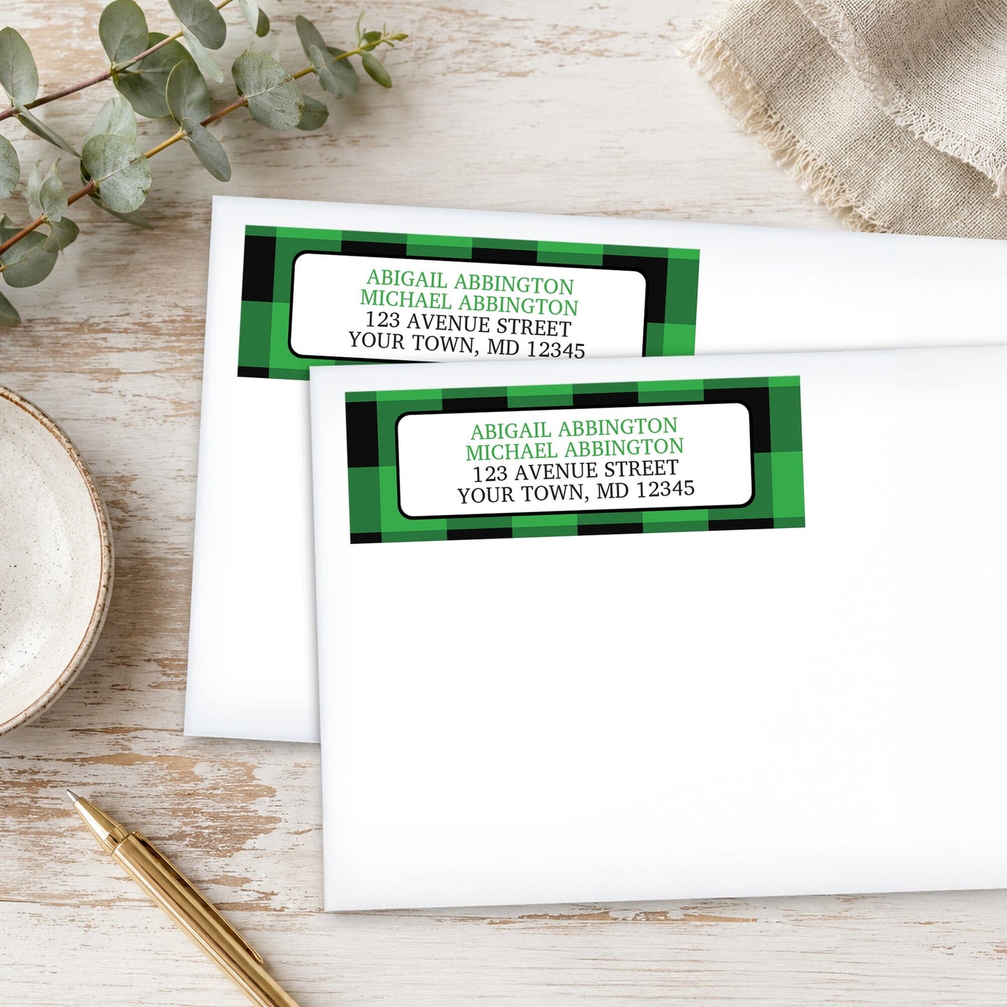Green and Black Buffalo Plaid Address Labels on white envelopes, shown on a wooden surface with plants and a pen.