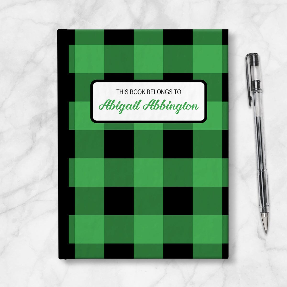 Personalized Green and Black Buffalo Plaid Journal at Artistically Invited. Image shows the book on a countertop next to a pen.