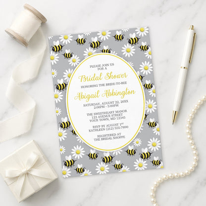 Happy Bee and Daisy Pattern Bridal Shower Invitation on a marble surface with a gift box, pen, and pearls.