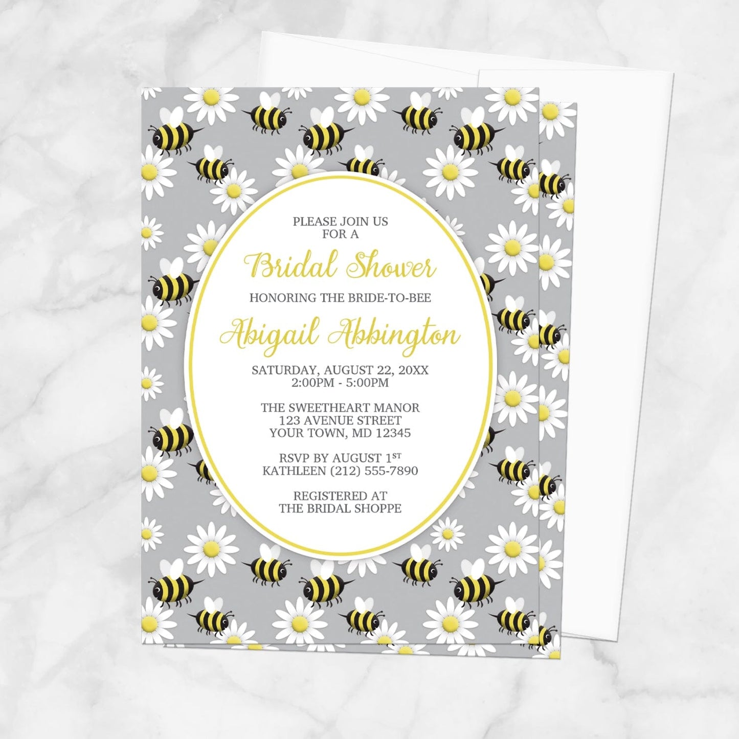 Bridal shower invitation with bee and daisy pattern on a gray background, displayed with a white envelope on a marble surface