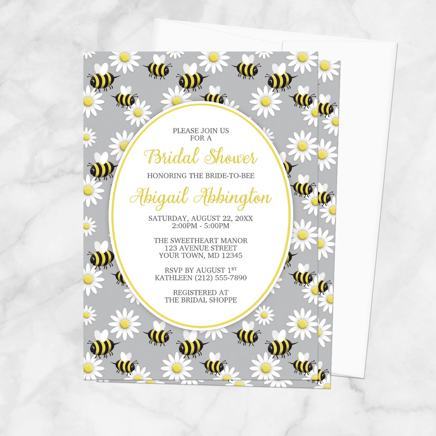 Bridal shower invitation with bee and daisy pattern on a gray background, displayed with a white envelope on a marble surface