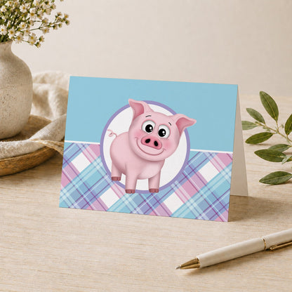 Happy Pig Pink Blue and Purple Plaid Note Card shown on a desk with a vase and a pen.