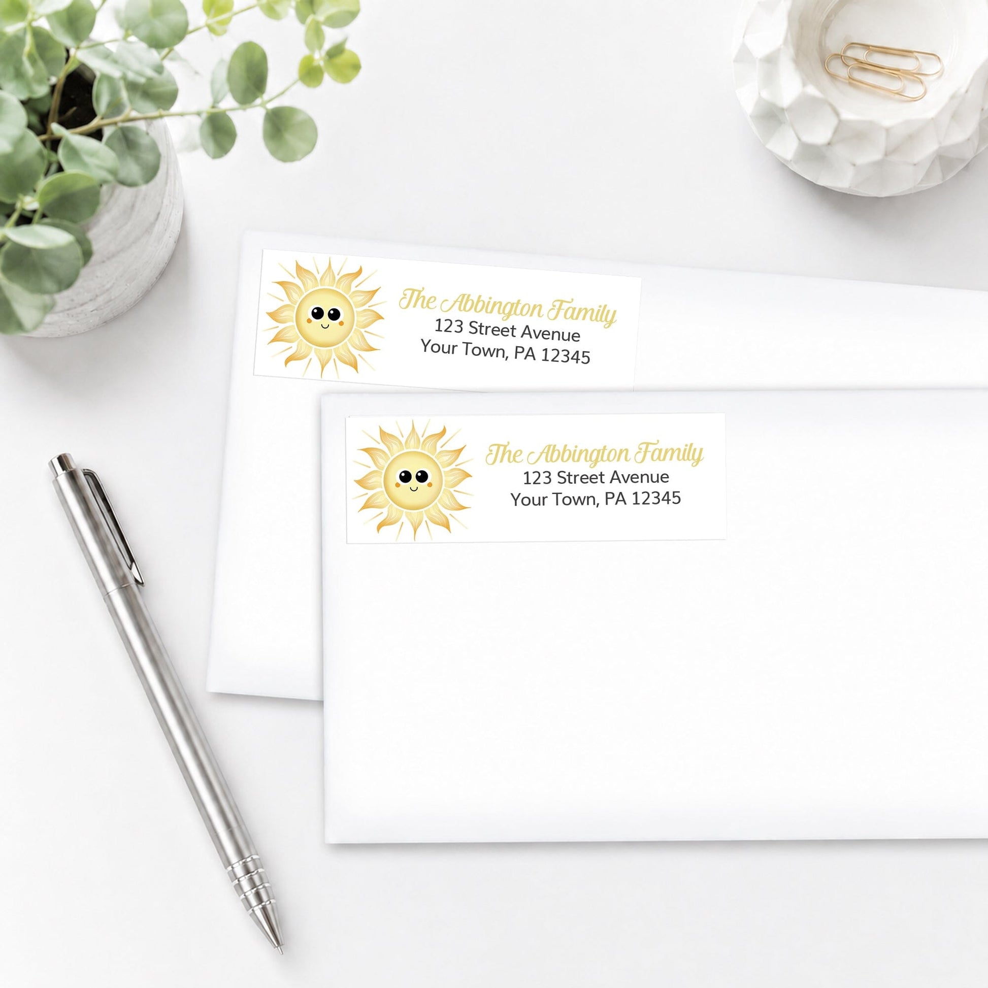 Happy Sun Address Labels on white envelopes shown on a white surface with a plant and a pen.
