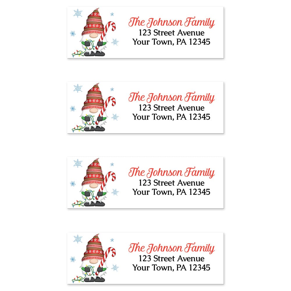 Holiday Candy Cane Gnome Address Labels at Artistically Invited. Sheet of 4 labels. These address labels are designed with an illustration of a cute gnome wearing a festive red hat while holding a large candy cane and a string of Christmas lights with snowflakes around him. Your personalized return address is custom printed in red and black over white to the right of the holiday-themed gnome.
