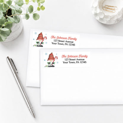 Two personalized Holiday Candy Cane Gnome Address Labels, shown on white envelopes, on a white surface with a pen and plant.