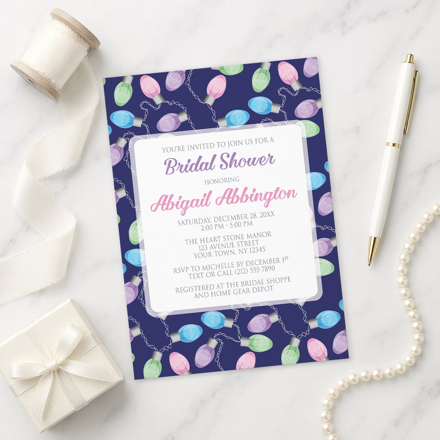 Holiday Lights Pattern Bridal Shower Invitation shown on a marble surface with a white gift box, pen, ribbon, and pearls.